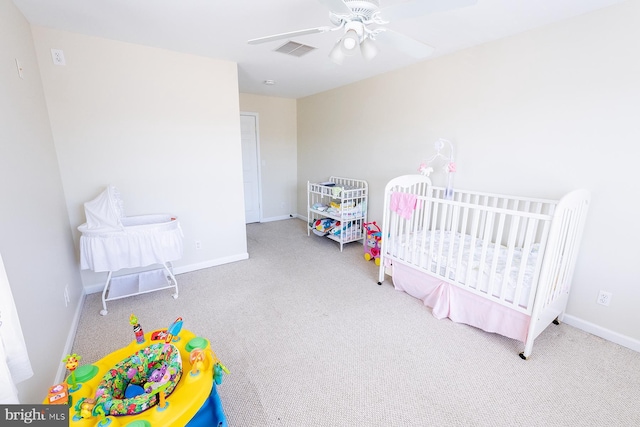 bedroom with ceiling fan, light colored carpet, and a crib