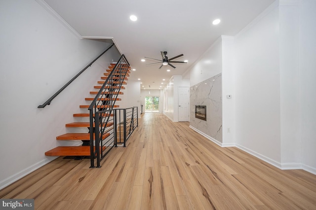 unfurnished living room featuring ceiling fan, a high end fireplace, ornamental molding, and light hardwood / wood-style flooring