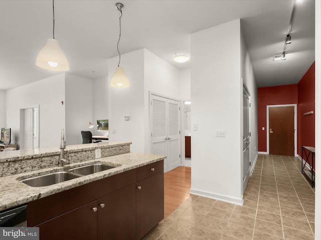 kitchen featuring track lighting, light stone counters, dark brown cabinetry, sink, and decorative light fixtures