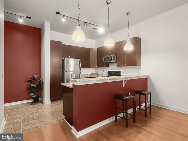 kitchen featuring light stone countertops, light wood-type flooring, dark brown cabinets, kitchen peninsula, and stainless steel appliances