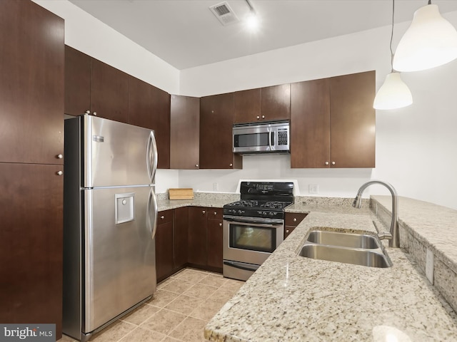 kitchen with sink, appliances with stainless steel finishes, decorative light fixtures, light stone counters, and dark brown cabinets