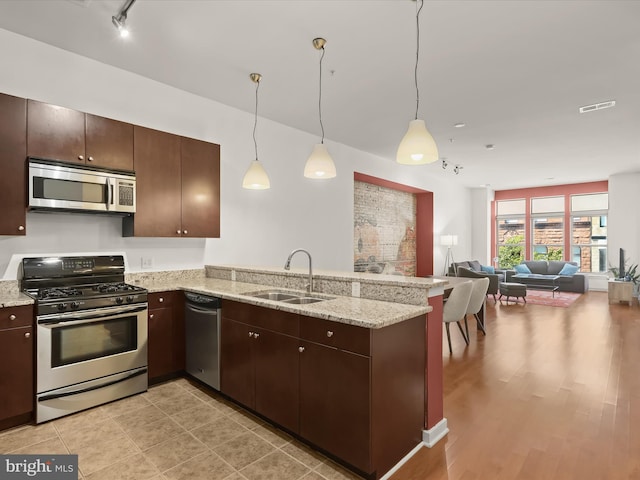 kitchen with kitchen peninsula, dark brown cabinetry, stainless steel appliances, sink, and pendant lighting