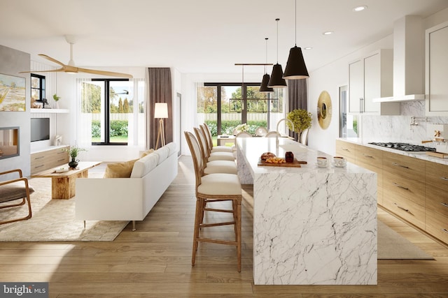 kitchen featuring wall chimney exhaust hood, backsplash, stainless steel gas stovetop, a center island with sink, and white cabinets