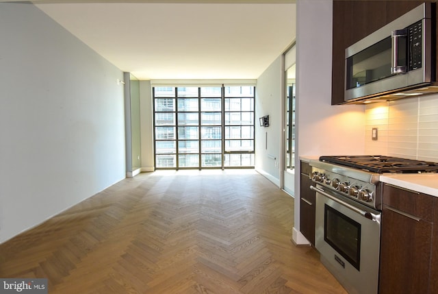 kitchen featuring appliances with stainless steel finishes, tasteful backsplash, dark brown cabinetry, light parquet flooring, and a wall of windows