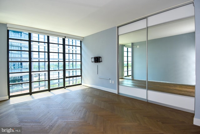 spare room with plenty of natural light, dark parquet flooring, and a wall of windows