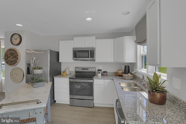 kitchen featuring light wood-type flooring, white cabinets, light stone counters, appliances with stainless steel finishes, and sink