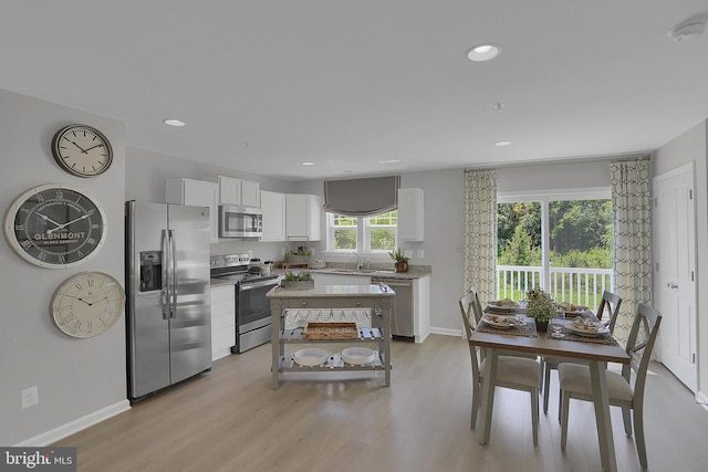 kitchen with stainless steel appliances, white cabinets, sink, light hardwood / wood-style floors, and a center island