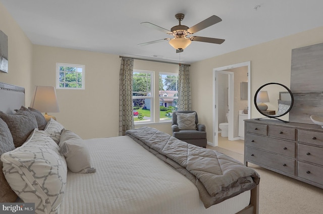 bedroom with ensuite bathroom, light colored carpet, and ceiling fan