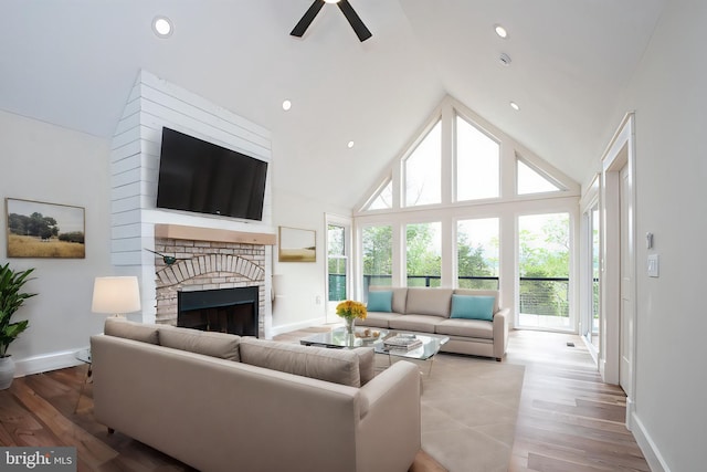 living room with wood-type flooring, high vaulted ceiling, a brick fireplace, and ceiling fan