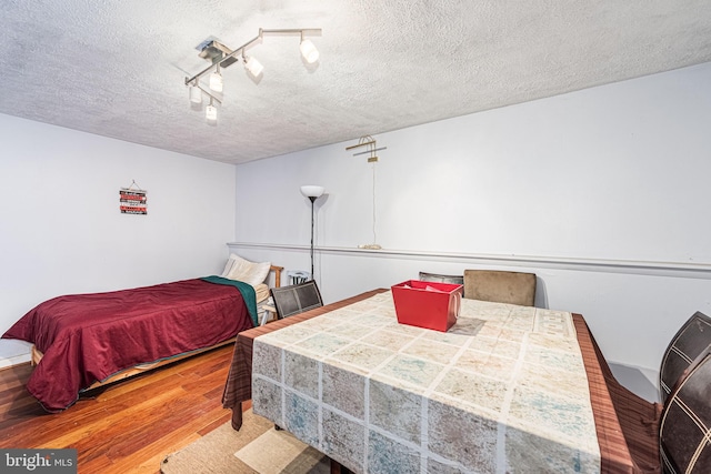 bedroom with a textured ceiling, hardwood / wood-style floors, and track lighting