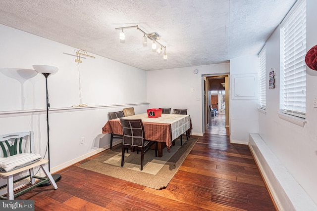 dining room featuring dark hardwood / wood-style floors, track lighting, and a textured ceiling