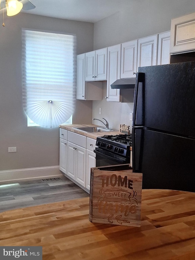 kitchen featuring sink, white cabinets, light hardwood / wood-style floors, black appliances, and plenty of natural light