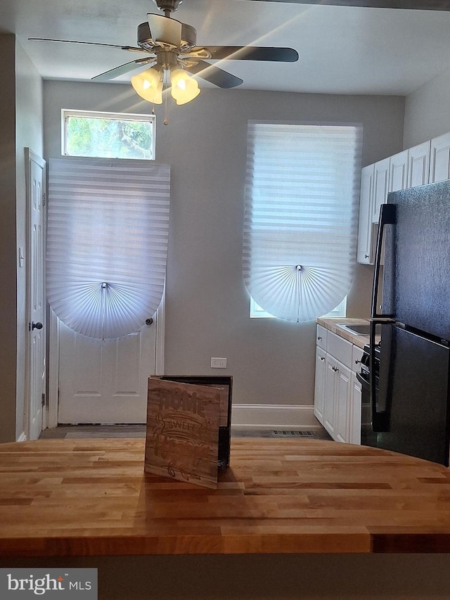 kitchen with black refrigerator, white cabinetry, ceiling fan, and light hardwood / wood-style floors