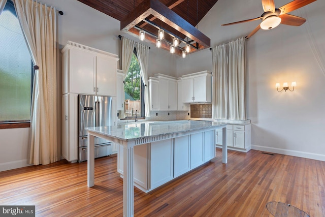 kitchen featuring a center island, tasteful backsplash, high end refrigerator, light stone counters, and white cabinets