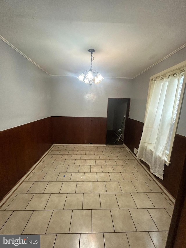 tiled empty room with a notable chandelier, wood walls, and ornamental molding