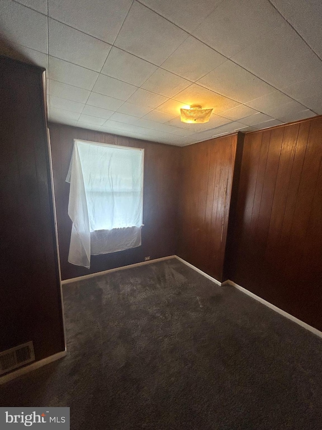 unfurnished room featuring wood walls and dark carpet