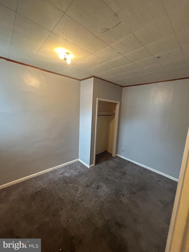 unfurnished bedroom with dark carpet, ornamental molding, and a closet