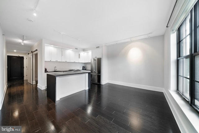 kitchen with stainless steel refrigerator, white cabinetry, a wealth of natural light, a barn door, and track lighting