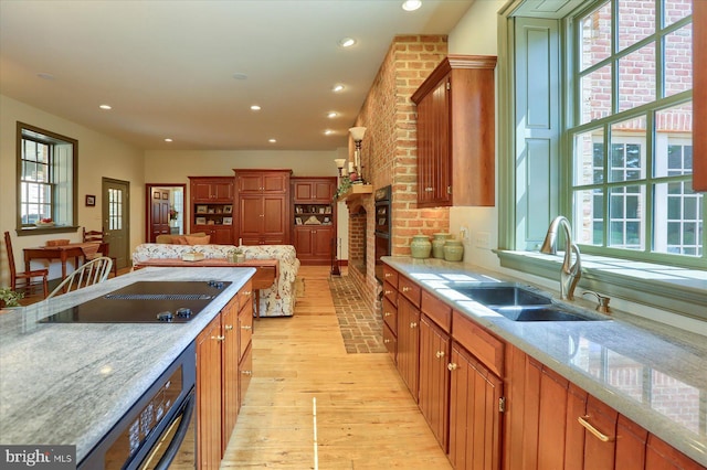 kitchen featuring light stone countertops, sink, a brick fireplace, black electric stovetop, and light wood-type flooring