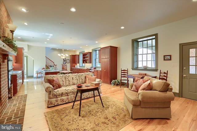 living room with a brick fireplace, light hardwood / wood-style floors, and an inviting chandelier