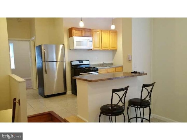 kitchen with a kitchen bar, kitchen peninsula, black gas range oven, and stainless steel refrigerator