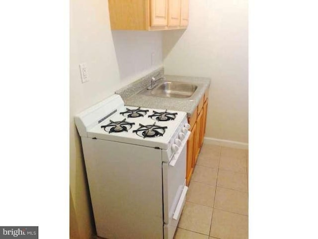 kitchen with light tile patterned flooring, light brown cabinetry, white gas stove, and sink