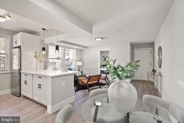 kitchen with kitchen peninsula, decorative light fixtures, white cabinets, light hardwood / wood-style floors, and stainless steel refrigerator