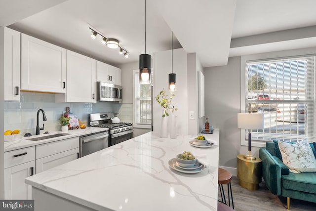 kitchen featuring hanging light fixtures, sink, light stone countertops, appliances with stainless steel finishes, and white cabinetry