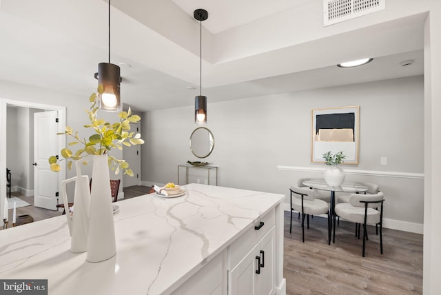 kitchen with light stone countertops, decorative light fixtures, white cabinetry, and light hardwood / wood-style flooring