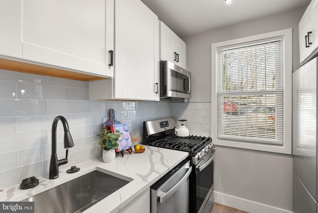 kitchen featuring sink, light stone counters, decorative backsplash, white cabinets, and appliances with stainless steel finishes