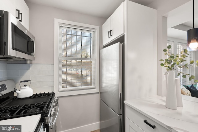 kitchen featuring light stone countertops, appliances with stainless steel finishes, tasteful backsplash, white cabinets, and hanging light fixtures