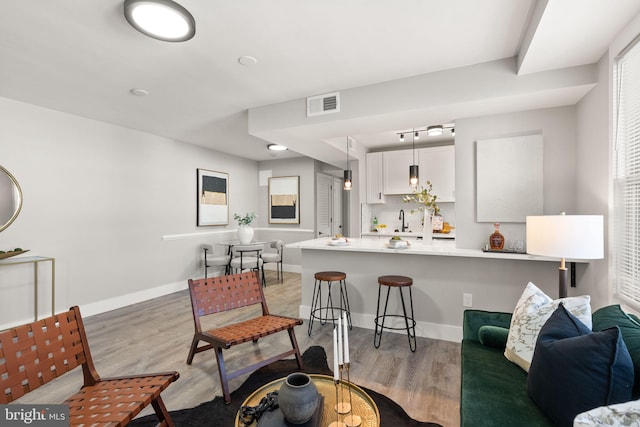 kitchen featuring kitchen peninsula, a kitchen breakfast bar, decorative light fixtures, white cabinets, and light hardwood / wood-style floors