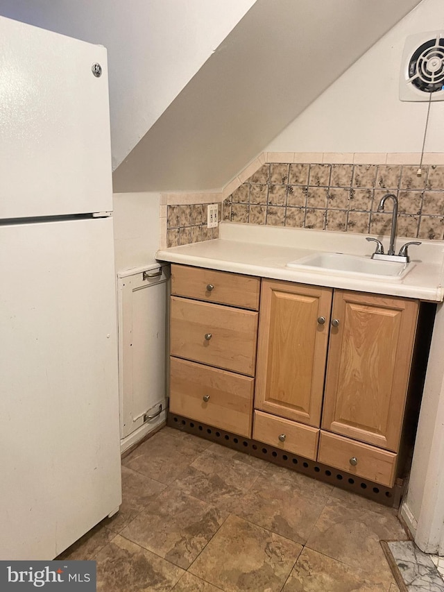 kitchen with white refrigerator, tasteful backsplash, vaulted ceiling, and sink