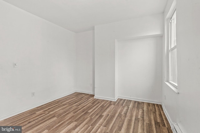 empty room featuring wood-type flooring and a baseboard radiator