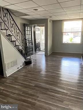 unfurnished living room with plenty of natural light, a drop ceiling, and dark hardwood / wood-style flooring