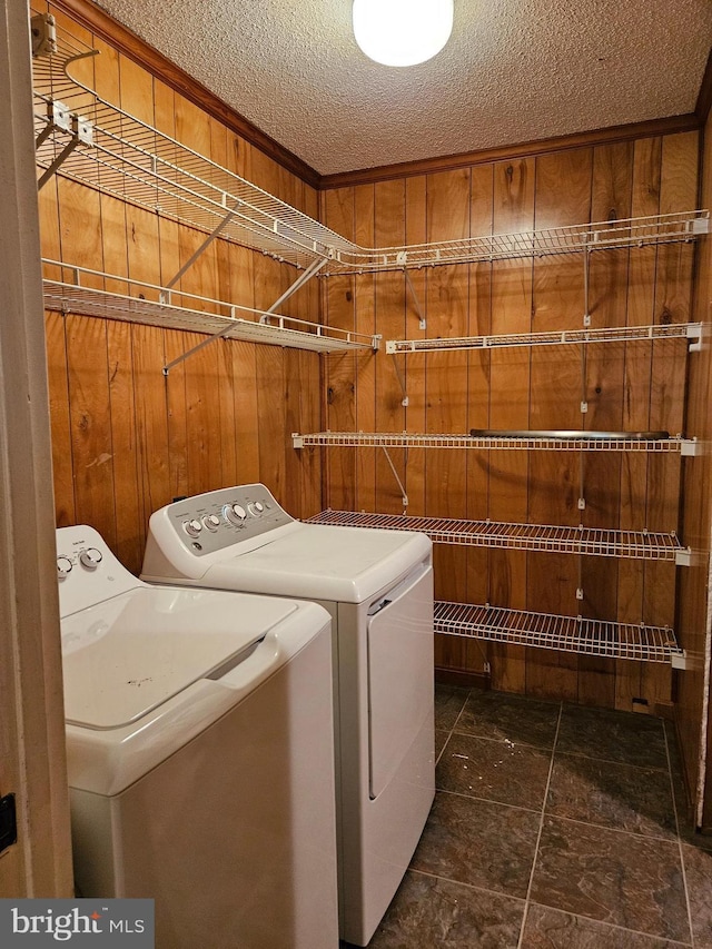 laundry room featuring washer and clothes dryer, wooden walls, and a textured ceiling