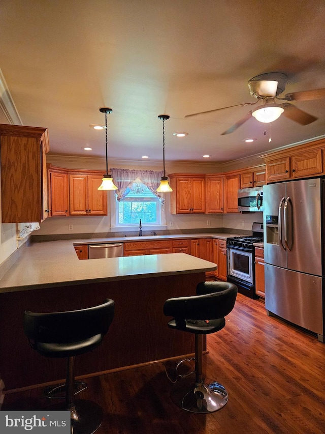 kitchen with appliances with stainless steel finishes, dark hardwood / wood-style floors, decorative light fixtures, a kitchen breakfast bar, and crown molding