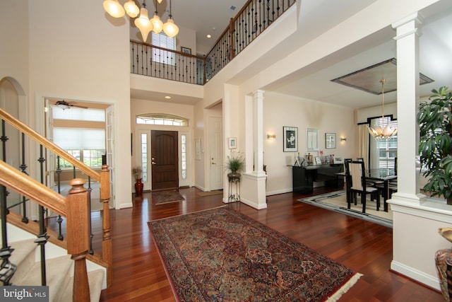 entryway featuring dark hardwood / wood-style flooring, a towering ceiling, decorative columns, crown molding, and an inviting chandelier