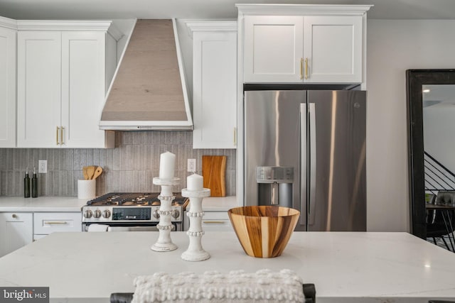 kitchen with white cabinets, custom exhaust hood, stove, and stainless steel refrigerator with ice dispenser