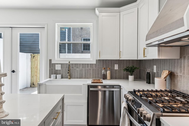 kitchen featuring white cabinetry, backsplash, light stone counters, stainless steel appliances, and wall chimney exhaust hood