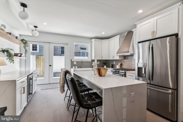 kitchen with appliances with stainless steel finishes, pendant lighting, premium range hood, backsplash, and hardwood / wood-style flooring