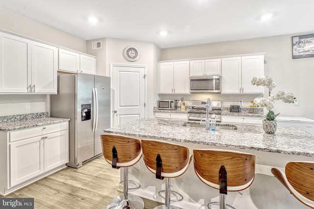 kitchen featuring light stone countertops, stainless steel appliances, sink, light hardwood / wood-style flooring, and white cabinets