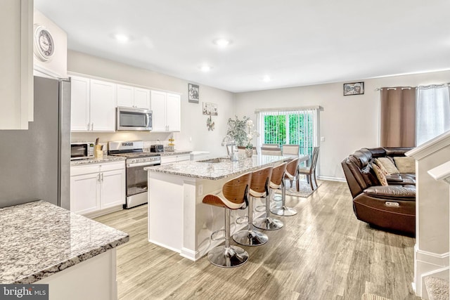 kitchen with light stone countertops, stainless steel appliances, sink, a center island with sink, and white cabinetry