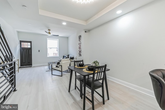 dining space featuring ceiling fan, light wood-type flooring, and a tray ceiling