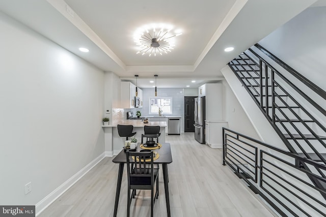 dining space featuring a tray ceiling, sink, light hardwood / wood-style floors, and a notable chandelier