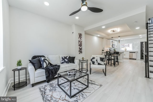 living room with a tray ceiling, ceiling fan, light hardwood / wood-style floors, and sink