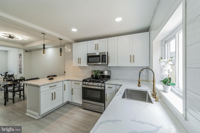 kitchen with sink, kitchen peninsula, decorative light fixtures, white cabinetry, and stainless steel appliances