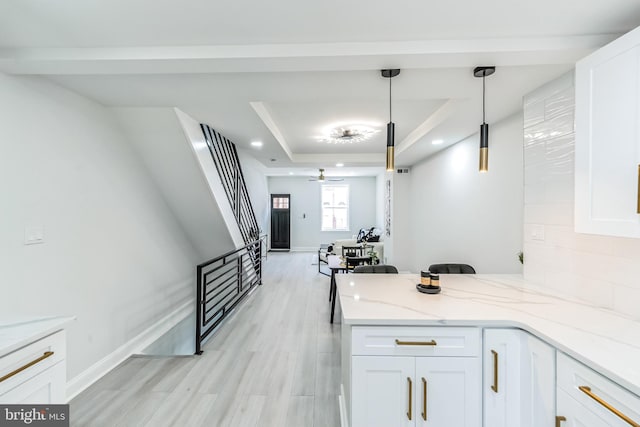 kitchen featuring light stone counters, a tray ceiling, ceiling fan, white cabinets, and hanging light fixtures