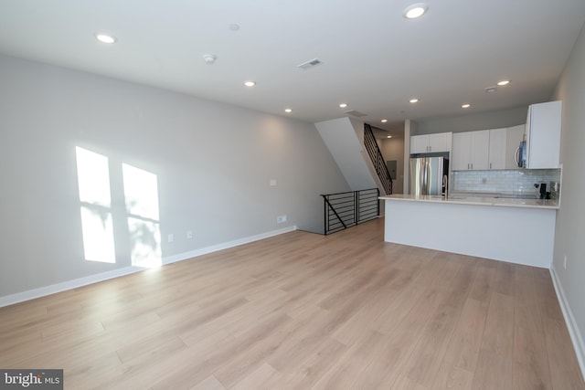 kitchen with white cabinetry, appliances with stainless steel finishes, light hardwood / wood-style flooring, and backsplash