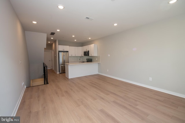 kitchen with white cabinets, backsplash, kitchen peninsula, stainless steel appliances, and light hardwood / wood-style flooring